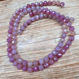 May include: A strand of faceted amethyst beads in shades of purple and pink. The beads are strung on a clear elastic cord.