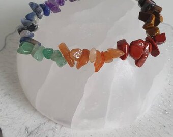 Op de afbeelding: Een regenboogkristallen armband gemaakt van kleine, onregelmatig gevormde stenen. De armband ligt op een wit, getextureerd oppervlak.