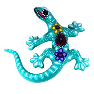Könnte beinhalten: Türkisfarbene Eidechsenfigur mit weißen Tupfen und floralen Designs in Gelb, Lila und Kastanienbraun. Die Eidechse hat einen langen Schwanz und ist glänzend lackiert. Die Figur ist ein dekorativer Gegenstand.