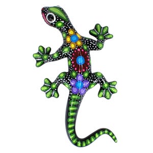 Peut inclure: Une figurine de lézard décorative peinte à la main. Le lézard noir est orné de pois blancs et de motifs floraux colorés jaunes, bleus, violets et rouges. Les pieds et la queue sont verts, et les yeux sont noirs et blancs.
