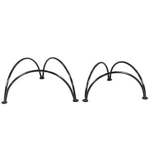 Op de afbeelding: Twee zwarte metalen plantenstandaards met een gebogen ontwerp. Elke standaard heeft drie poten en een reeks bogen. De standaards zijn ontworpen om planten of andere decoratieve items te verhogen.