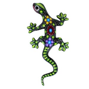 Könnte beinhalten: Handbemalte Eidechsenfigur aus Holz. Die Eidechse ist schwarz mit weißen Punkten und bunten Blumenmustern in Gelb, Rot und Lila. Die Füße und der Schwanz der Eidechse sind grün.