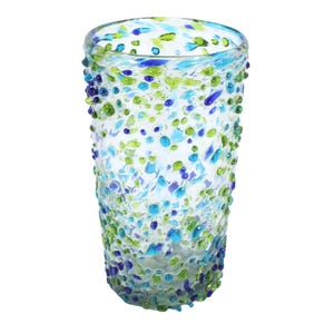 Könnte beinhalten: Ein klarer Glasbecher mit einem gesprenkelten Design. Das Glas ist mit blauen, grünen und lila Punkten verziert, wodurch ein strukturiertes Aussehen entsteht. Der zylindrische Becher scheint handgefertigt zu sein.