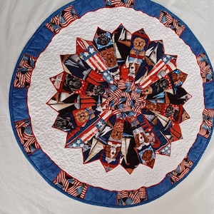 Peut inclure: Un chemin de table rond en coton matelassé blanc avec une bordure bleue et rouge. Le centre du chemin de table présente un motif en étoile avec des images de chiens et de drapeaux américains.
