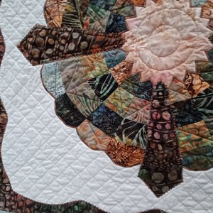 Peut inclure: Une courtepointe blanche avec un motif de patchwork brun et vert au centre. Le patchwork a la forme d'une fleur avec un centre rose clair. La courtepointe est matelass&eacute;e avec un motif en losange.