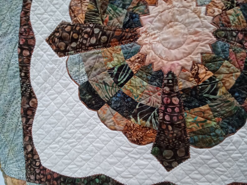 Peut inclure: Une courtepointe blanche avec un motif de patchwork brun et vert au centre. Le patchwork a la forme d'une fleur avec un centre rose clair. La courtepointe est matelass&eacute;e avec un motif en losange.