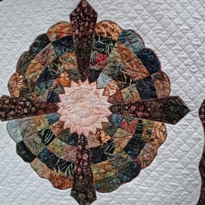 Peut inclure: Une courtepointe blanche avec un motif brun et bleu au centre. Le motif est un cercle avec un &eacute;clat d'&eacute;toile au milieu. La courtepointe est matelass&eacute;e avec un motif en losange.