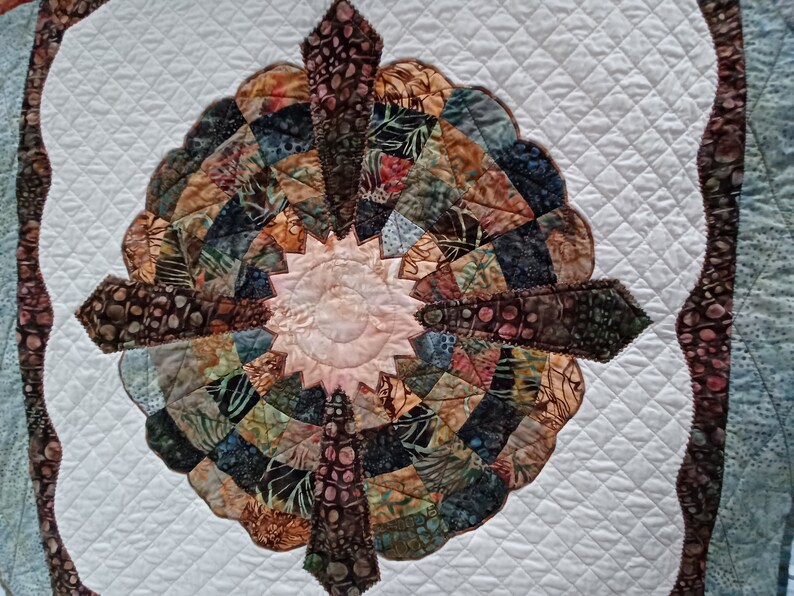 Peut inclure: Une courtepointe blanche avec un motif brun et bleu au centre. Le motif est un cercle avec un &eacute;clat d'&eacute;toile au milieu. La courtepointe est matelass&eacute;e avec un motif en losange.