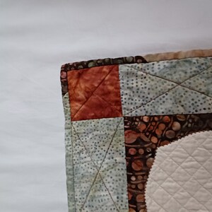 Peut inclure: Un gros plan sur un coin de courtepointe avec un motif de patchwork. La courtepointe est faite de diff&eacute;rents tissus dans des tons de brun, de vert et de blanc. Le tissu est matelass&eacute; avec un motif en losange.