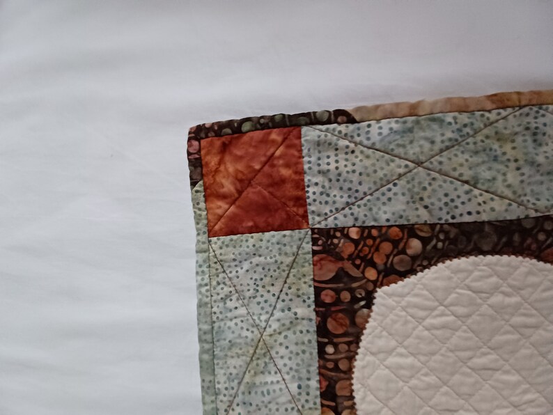 Peut inclure: Un gros plan sur un coin de courtepointe avec un motif de patchwork. La courtepointe est faite de diff&eacute;rents tissus dans des tons de brun, de vert et de blanc. Le tissu est matelass&eacute; avec un motif en losange.