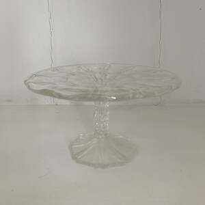 May include: A clear glass cake stand with a scalloped edge and a pedestal base.