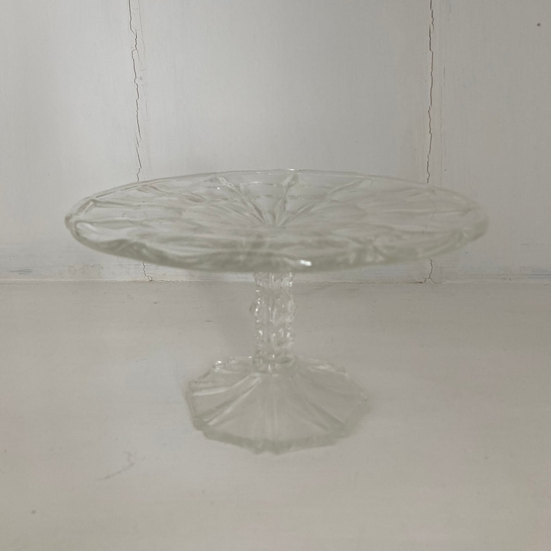 May include: A clear glass cake stand with a scalloped edge and a pedestal base.