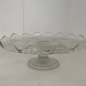 May include: A clear glass cake stand with a scalloped edge and a pedestal base.