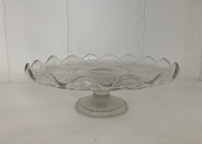 May include: A clear glass cake stand with a scalloped edge and a pedestal base.