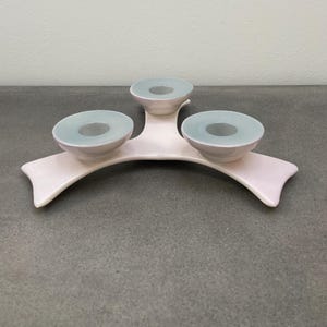 May include: A white ceramic candle holder with three teal-coloured candle cups. The holder is shaped like a tree branch with three curved arms.