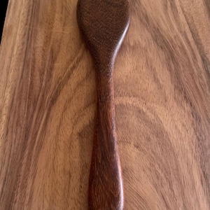 May include: A dark brown wooden spoon with a rounded bowl and a long, slender handle.