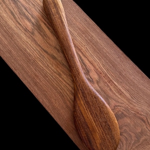 May include: A wooden spoon with a dark brown colour and a natural wood grain pattern. The spoon has a long handle and a rounded bowl.