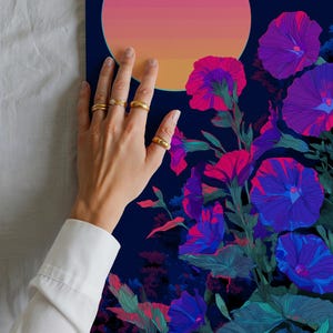 May include: A vibrant floral art print featuring stylized morning glory flowers in shades of purple, pink, and blue against a dark blue background. A gradient of pink and orange suggests a sunset or sunrise. Gold rings adorn the fingers.