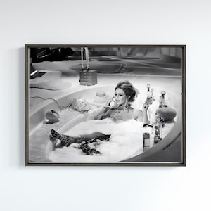 May include: A black and white photograph of a woman in a bathtub, talking on a phone. She is surrounded by bubbles and has a relaxed expression on her face.