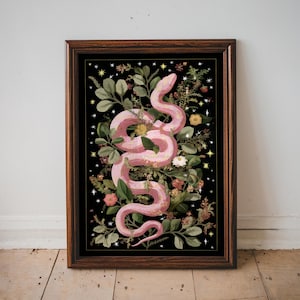Puede incluir: Una impresión artística enmarcada que presenta una serpiente rosa enroscada entre exuberante vegetación y flores sobre un fondo negro. La obra de arte incluye flores amarillas y blancas, con estrellas. El marco es de color marrón oscuro.