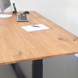 Könnte beinhalten: Ein heller Holztisch mit einem schwarzen, verstellbaren Bein. Auf dem Tisch liegen ein weißer Notizblock und ein blauer Stift.