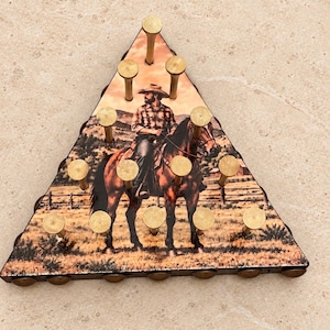 May include: A triangular wooden peg game board featuring a printed image of a person in a cowboy hat riding a brown horse in a field. The board has fifteen holes, each containing a brass-colored metal peg arranged in a pyramid pattern.