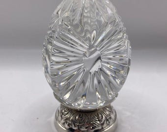Könnte beinhalten: Ein klares Kristallei mit einem geschliffenen Glasdesign sitzt auf einem verzierten silbernen Sockel.