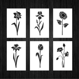 May include: Six black and white floral art prints. Each print features a different flower silhouette: daffodil, iris, sunflower, tulip, and poppy. The prints are displayed on a dark wood background.