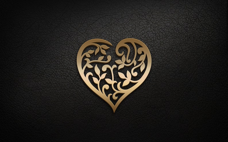 May include: A gold heart-shaped design with intricate floral patterns cut out of the metal. The heart is on a black leather background.