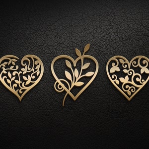 May include: Three gold-colored metal hearts with intricate floral designs. The hearts are arranged horizontally on a black textured background.