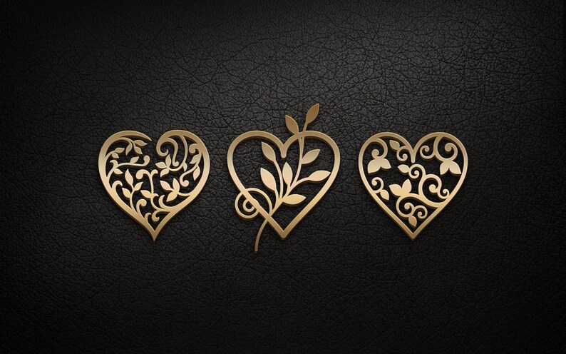 May include: Three gold-colored metal hearts with intricate floral designs. The hearts are arranged horizontally on a black textured background.