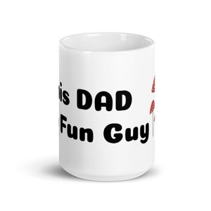 Könnte beinhalten: Weiße Keramik-Kaffeetasse mit schwarzem Text "This Dad is a Fun Guy" und einer roten und weißen Pilzgrafik.