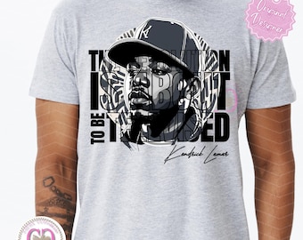 May include: A gray t-shirt with a black and white graphic of a man wearing a baseball cap. The graphic includes the text "The revolution is about to be televised" and the signature "Kendrick Lamar".