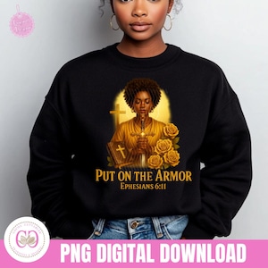 May include: Black sweatshirt featuring a graphic of a person holding a sword, with a cross and roses. Text reads "PUT ON THE ARMOR Ephesians 6:11". The design is in shades of gold and brown.