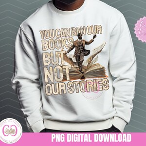 May include: White sweatshirt with a graphic design of a man standing on a book with the text "You can ban our books but not our stories".