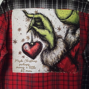 May include: Red and black plaid flannel shirt with a Grinch graphic on the back. The graphic shows the Grinch's green hand holding a red heart ornament. The text on the graphic reads, "Maybe Christmas, perhaps, means a little bit more."