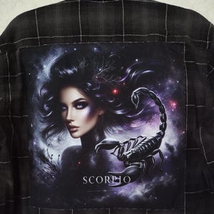 May include: A black and white plaid shirt with a patch featuring a woman with long black hair and a scorpion. The patch has a starry background and the word "SCORPIO" printed in white.