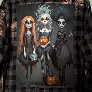 May include: A black and gray plaid flannel shirt with a bleached effect, featuring a large rectangular patch on the back. The patch displays three stylized female figures with long hair, wearing dark dresses and holding carved jack-o'-lanterns.