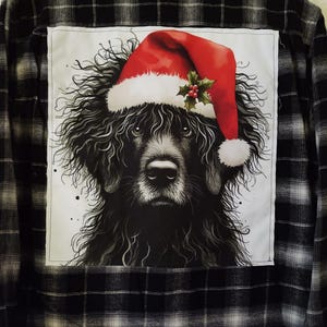 May include: A black and white plaid flannel shirt with a patch on the back. The patch features a black dog wearing a red Santa hat with a green holly sprig.