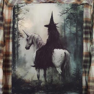 May include: A long-sleeved flannel shirt with a plaid pattern in shades of brown, tan, and cream. The back of the shirt features a dark, artistic print of a witch riding a unicorn through a forest.