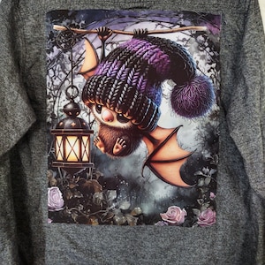 May include: A purple and black knitted hat with a pom-pom on top is worn by a small, furry creature with wings. The creature is holding onto a branch and a lantern is hanging from the branch. The background is a dark forest with roses.