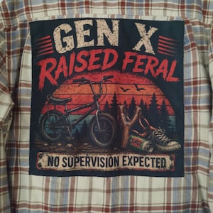 May include: A beige, blue, and red plaid flannel shirt featuring a large rectangular back patch. The patch displays a graphic of a BMX bike, a slingshot, a soda can, and a sneaker with the text GEN X RAISED FERAL and NO SUPERVISION EXPECTED.