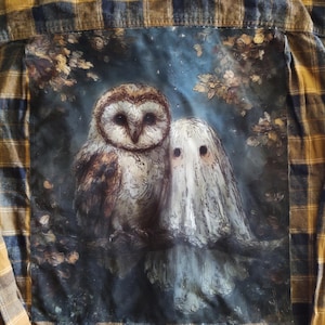 May include: A flannel shirt with a large, centered graphic featuring an owl and a ghost-like figure. The owl is brown and white, and the ghost is white. The shirt has a plaid pattern in shades of yellow, brown, and blue.