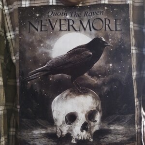 May include: Brown plaid hooded shirt with a large graphic on the back. The graphic features a black raven perched on a skull, with the words "Quoth The Raven NEVERMORE" against a starry night sky background.