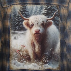 May include: A blue and tan plaid flannel shirt with a large patch on the back featuring a white Highland cow in a snowy forest scene. The cow has long horns and shaggy fur. The patch is stitched onto the shirt.