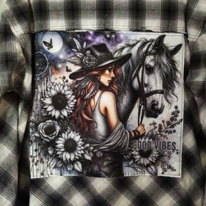 May include: A black and white illustration of a woman with long red hair wearing a hat and riding a white horse. The background is a galaxy with stars and a dreamcatcher. The text "GOOD VIBES" is written on the bottom of the image.