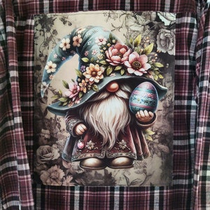 May include: A red and black plaid flannel shirt with a patch pocket featuring a gnome wearing a floral hat and holding a colorful Easter egg.