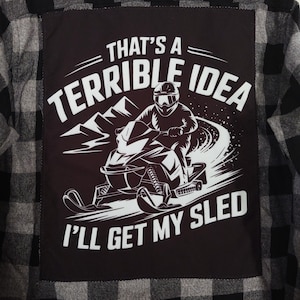 May include: Black and gray plaid flannel shirt with a black patch featuring a snowmobile graphic and the text "That's a Terrible Idea, I'll Get My Sled" in white. The shirt has a classic button-down design.