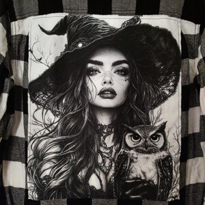 May include: Black and white plaid flannel shirt with a graphic of a witch wearing a hat and an owl. The witch has long hair and is wearing a necklace. The owl is perched on her shoulder.