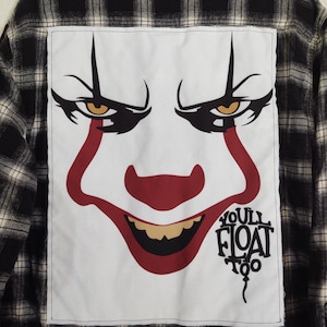 May include: Black and white plaid flannel shirt with a large white square on the back featuring a clown face graphic. The clown has red lips, a red nose, and the text "YOU'LL FLOAT TOO".